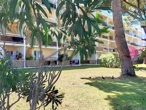 A multi-story building with balconies, surrounded by greenery and a grassy area.