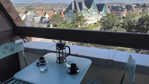 A balcony with a table set for two, a kettle, and a cup. The view includes a town with houses and a hill in the distance. - Cabourg: Renovated Duplex 2P, Direct Beach, Fiber (Cabourg)