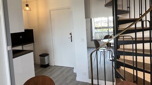 A modern kitchen with a built-in oven, a dining area with a table and chairs, and a staircase leading to an upper level. - Cabourg: Renovated Duplex 2P, Direct Beach, Fiber (Cabourg)