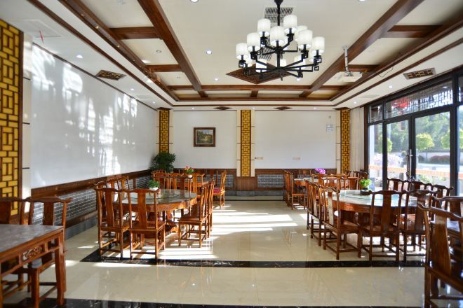 A spacious dining area with multiple wooden tables and chairs, a chandelier, and large windows.