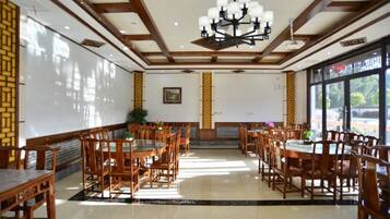 A spacious dining area with multiple wooden tables and chairs, a chandelier, and large windows.