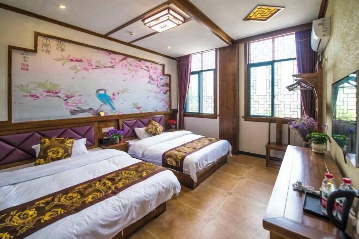 A hotel room with two beds, a large wall painting, a desk with a chair, and a window with curtains.