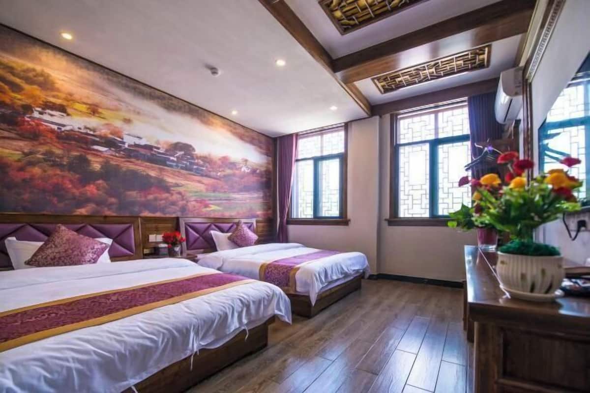 A hotel room with two beds, a large wall mural, wooden flooring, and a window with a view.