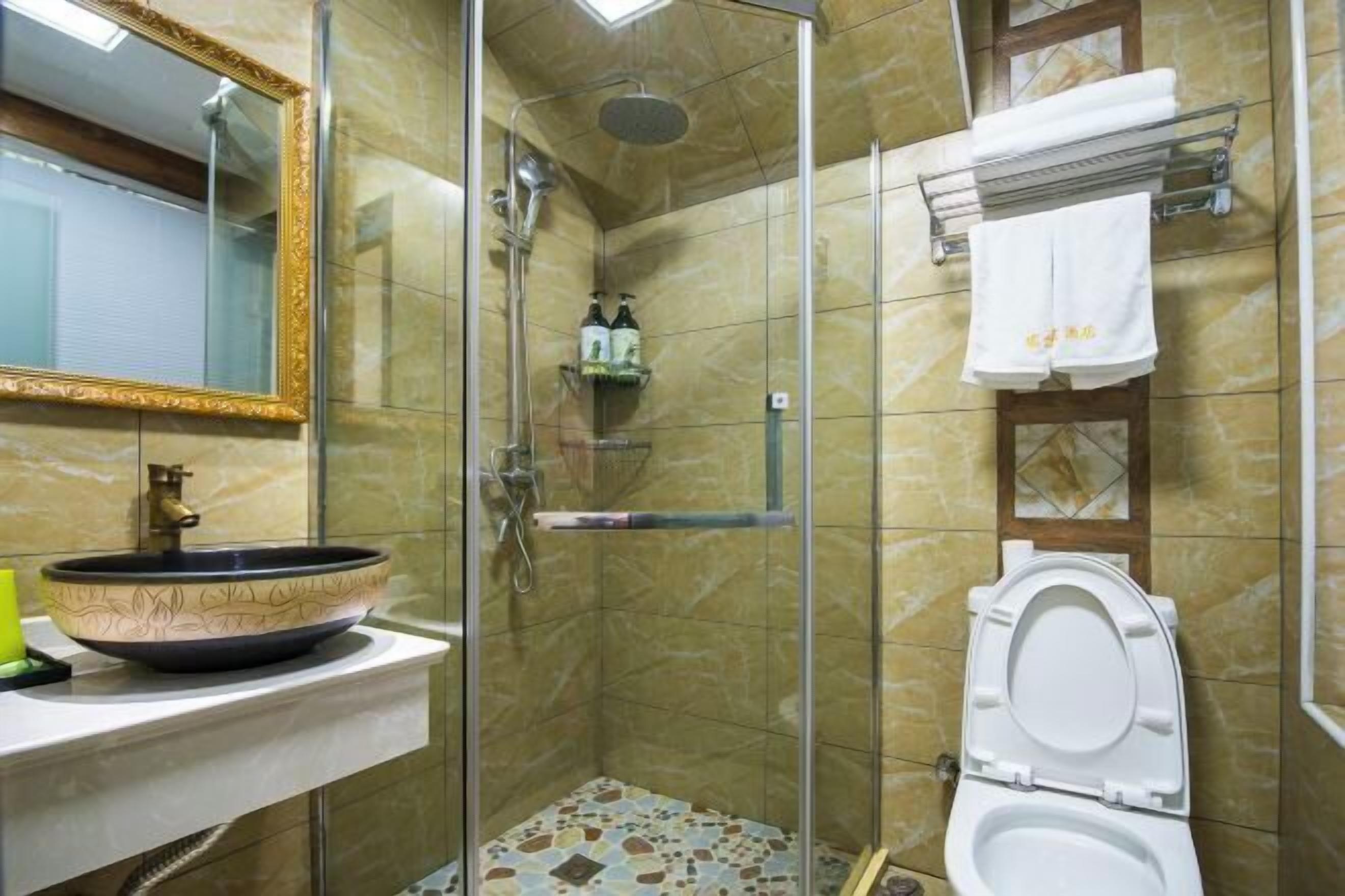 A bathroom with a glass-enclosed shower, a sink with a decorative bowl, a toilet, and a mirror with a gold frame.