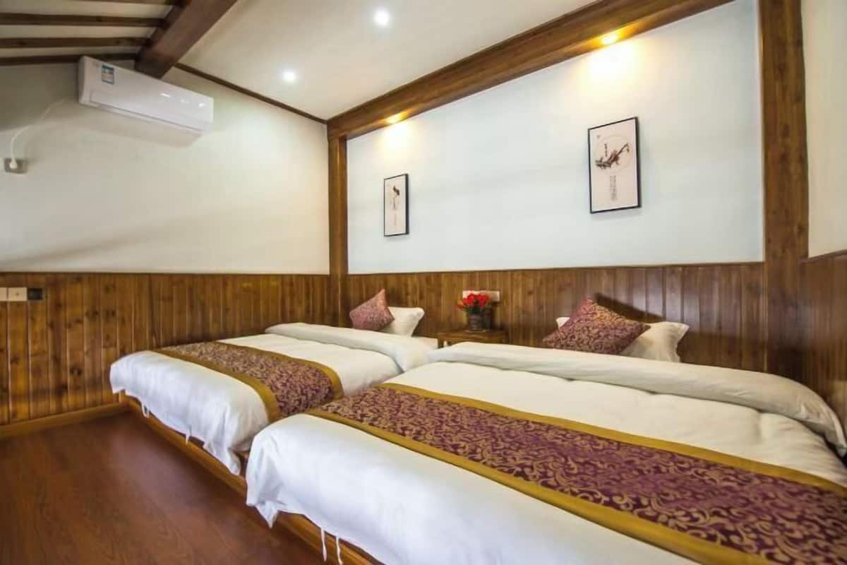 A hotel room with two beds, wooden paneling, a wall-mounted air conditioner, and framed artwork.