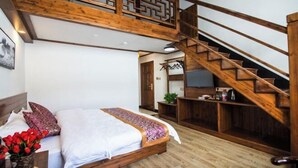 A bedroom with a wooden staircase, a bed with a patterned bedspread, and a small table with a vase of flowers.