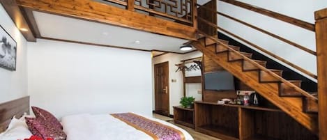 Un dormitorio con escalera de madera, cama con colcha estampada y una mesita con un florero.