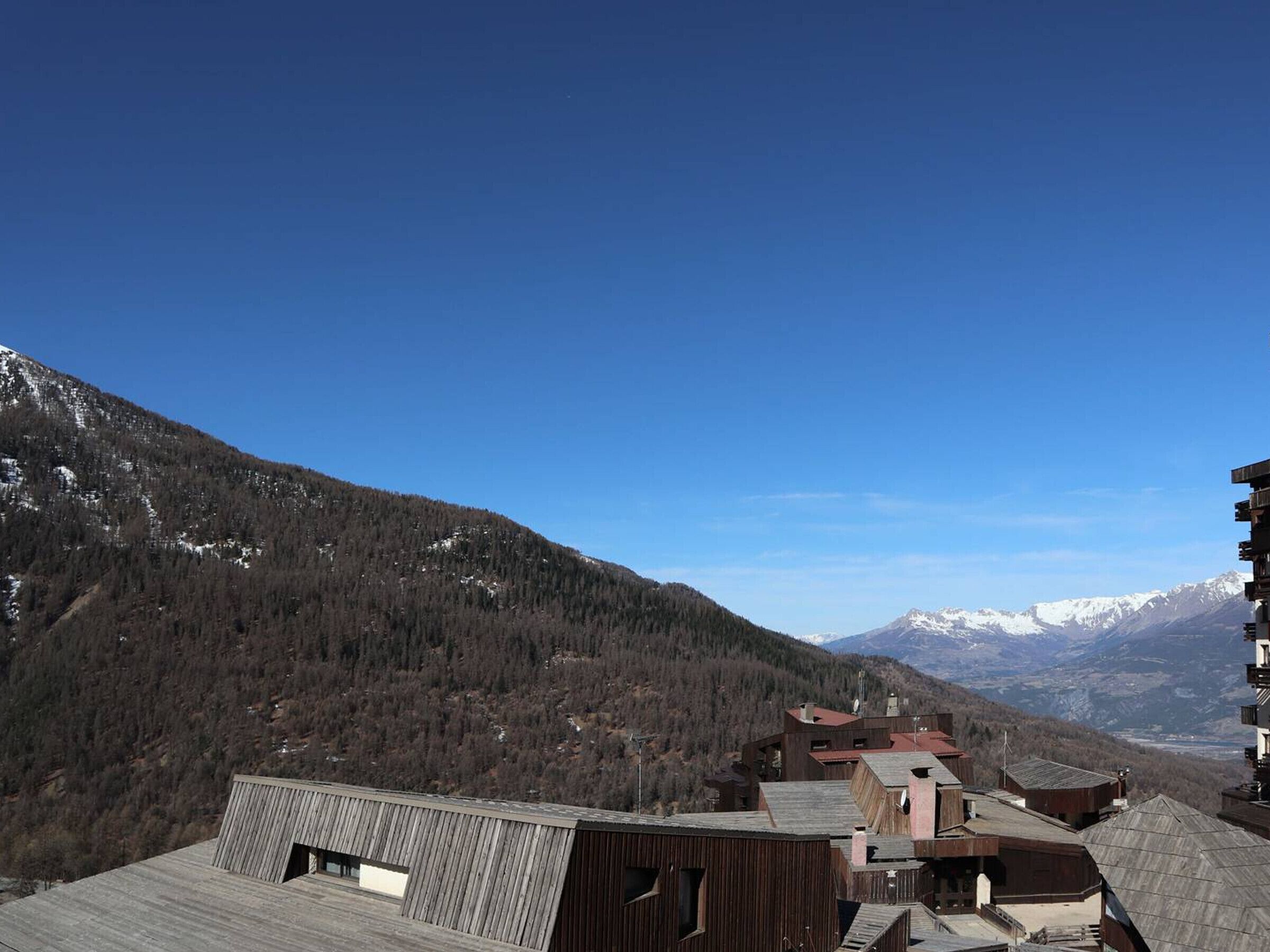 Un paisaje montañoso con cielo despejado. Se observan edificios con techos de madera y una mezcla de arquitectura moderna y tradicional.