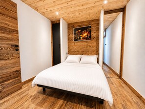 A bedroom with a wooden ceiling, a bed with white bedding, and a painting on the wall.