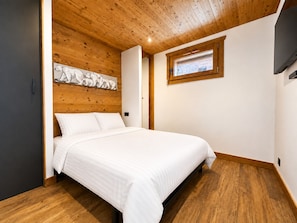 Een slaapkamer met een houten plafond, een bed met wit beddengoed, een raam met uitzicht en een aan de muur bevestigde televisie.