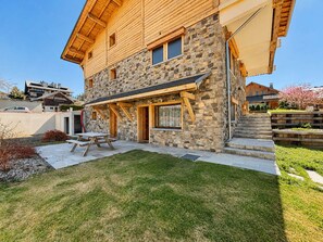Ein zweistöckiges Steinhaus mit einer Holzterrasse und einem kleinen Garten.
