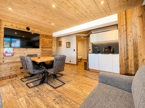 Ein modernes Interieur mit Holzbalkendecke, einem Essbereich mit Tisch und Stühlen, einer Küchenzeile mit Schränken und einem grauen Sofa.