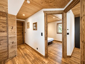 Ein Flur mit Holzboden, einem Bett im Hintergrund und gerahmten Bildern an der Wand.
