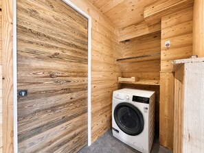 A compact laundry room with a washing machine, wooden walls, and a door.