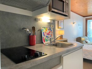 A compact kitchen with a microwave, a sink, and a red utensil holder.
