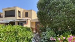 Un edificio in stile mediterraneo con tetto in tegole, circondato da vegetazione lussureggiante e piante fiorite.
