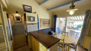 Una cucina compatta con zona pranzo, con tavolo e sedie in legno, forno a incasso e piccolo frigorifero.
