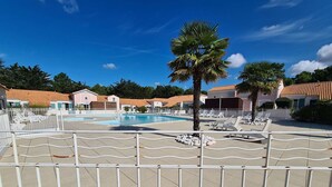 Un espace piscine doté d’une terrasse entourée d’une clôture, de chaises longues et de palmiers.