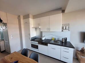 A modern kitchen with white cabinets, a black countertop, and a dining area with a wooden table and chairs.