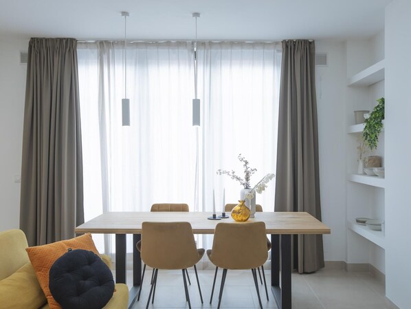Een eetruimte met een houten tafel, vier stoelen, een vaas met bloemen en een plank met decoratieve objecten.