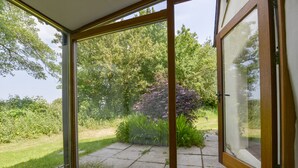 Een kamer met een glazen deur die uitkomt op een tuin met gazon, een pad en diverse planten.