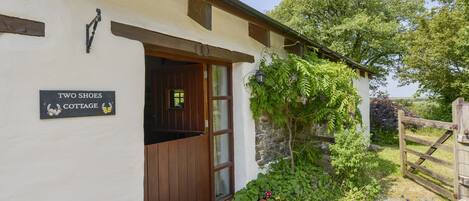 A cottage entrance with a wooden door and a sign reading 'TWO SHOES COTTAGE'.