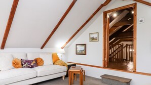 Een gezellig slaapkamer op zolder met een witte bank, houten balken, een klein houten tafeltje en een trap naar een entresol.