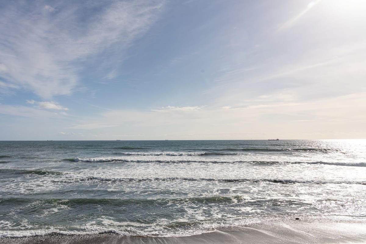 A beach with waves, a clear sky, and distant ships.