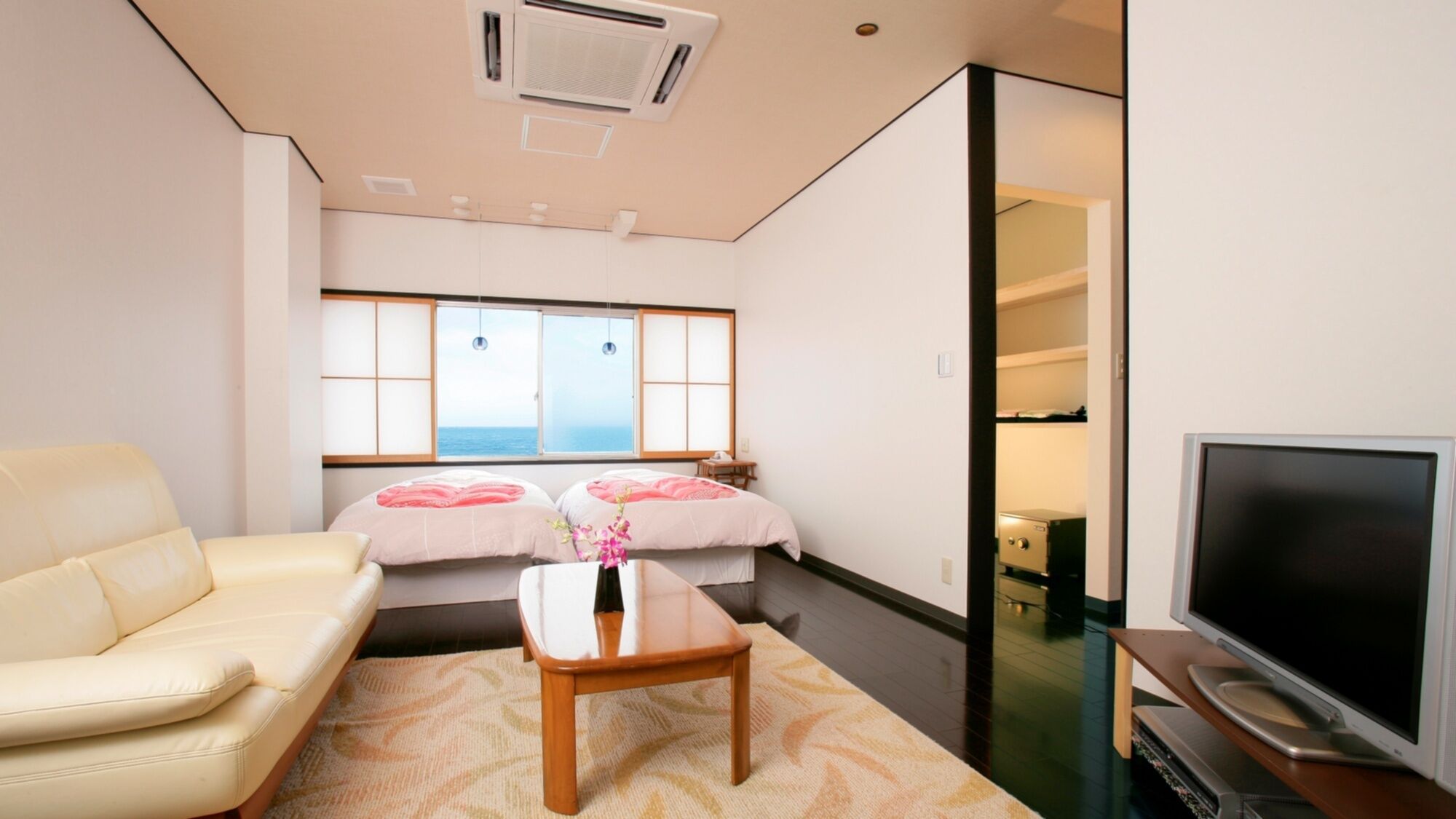 Une chambre d’hôtel avec un canapé, une petite table, une télévision, une fenêtre donnant sur un paysage agréable et une porte coulissante menant à un placard.