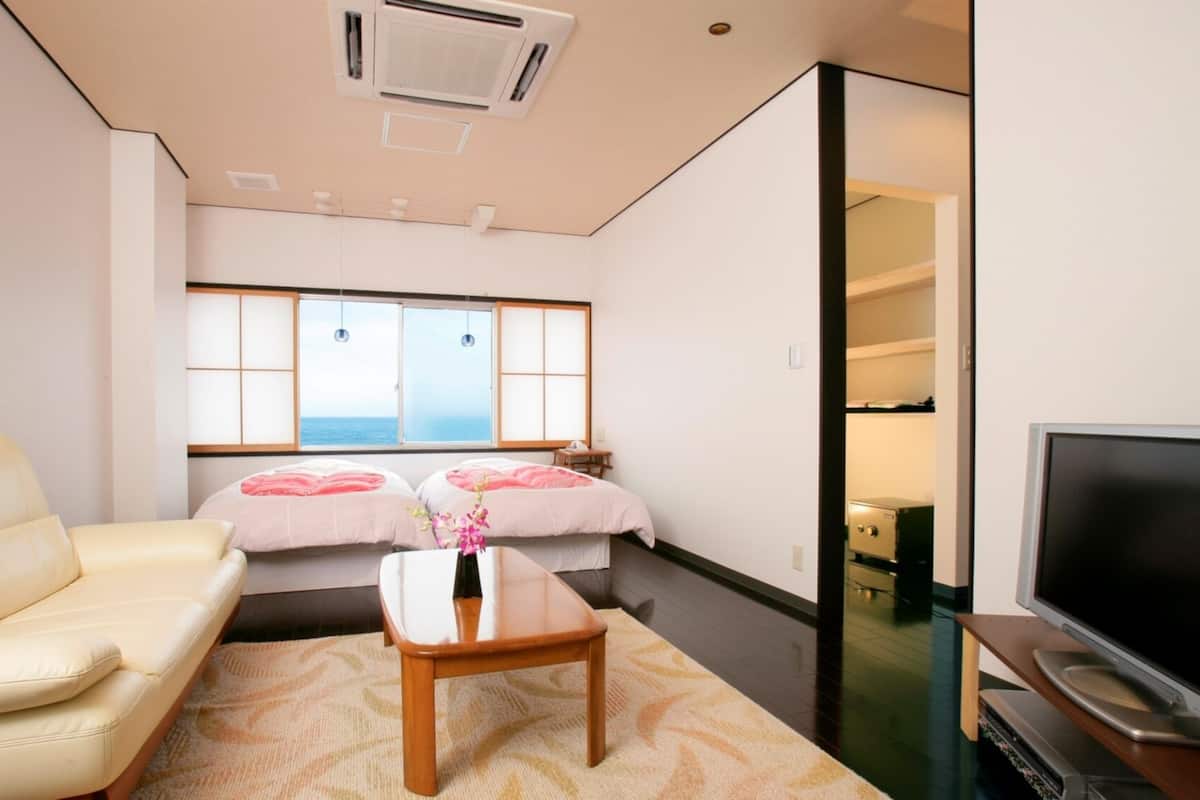 Une chambre d’hôtel avec un canapé, une petite table, une télévision, une fenêtre donnant sur un paysage agréable et une porte coulissante menant à un placard.