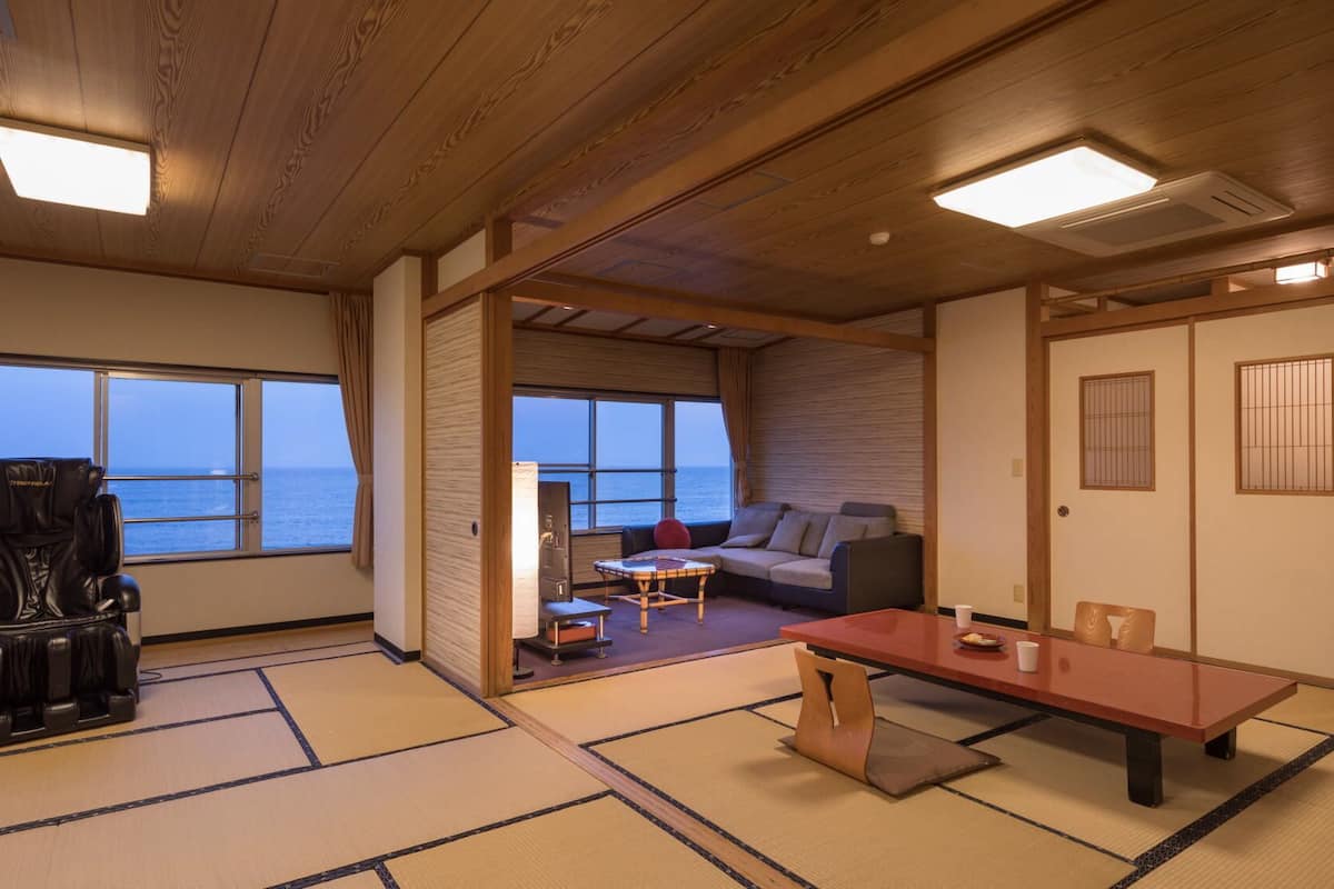 A room with tatami flooring, a sofa, a table, a massage chair, and a view of the sea.