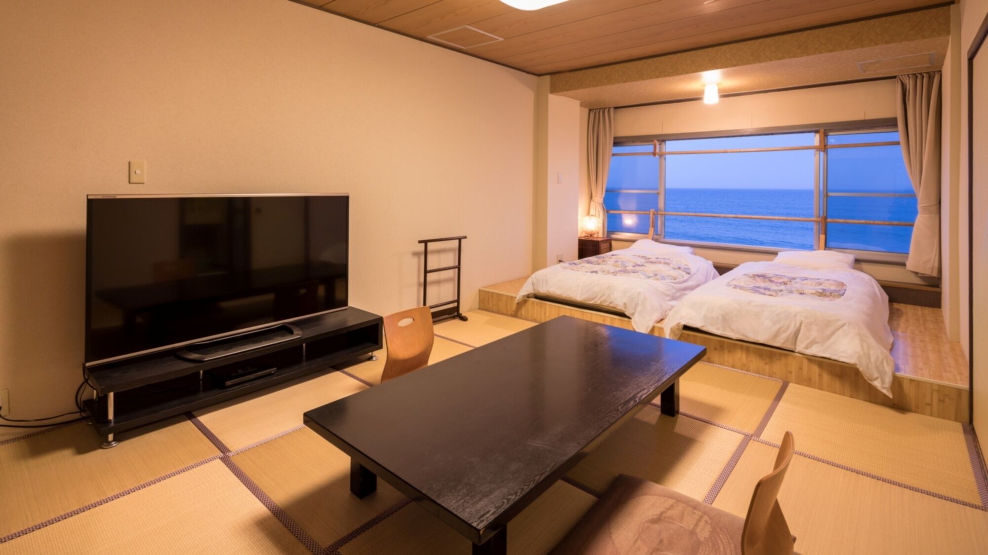 Une chambre avec une télévision, une table, deux lits, une fenêtre donnant sur un beau paysage et une lampe.