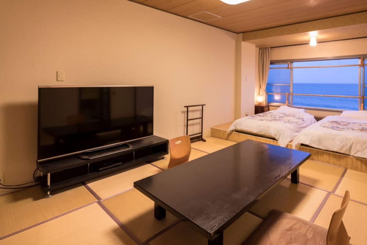 A room with a TV, a table, two beds, a window with a view, and a lamp.