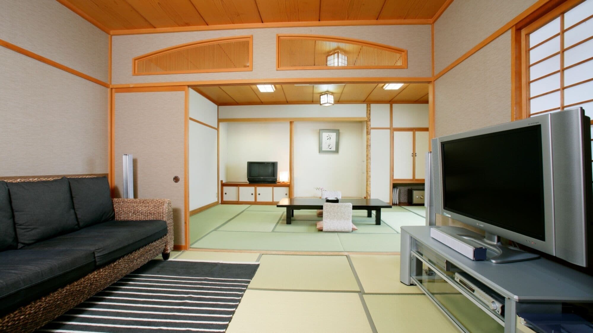 Un salon de style japonais traditionnel, avec un sol recouvert de tatamis, une table basse, un canapé et un téléviseur.