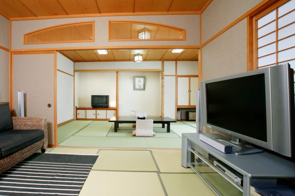 Un salon de style japonais traditionnel, avec un sol recouvert de tatamis, une table basse, un canapé et un téléviseur.