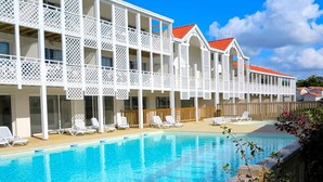 Un hotel con piscina, balcones de celosía blanca y techos rojos.