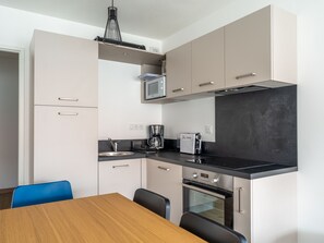 A modern kitchen with a microwave, coffee maker, and oven. There is a dining table with chairs.