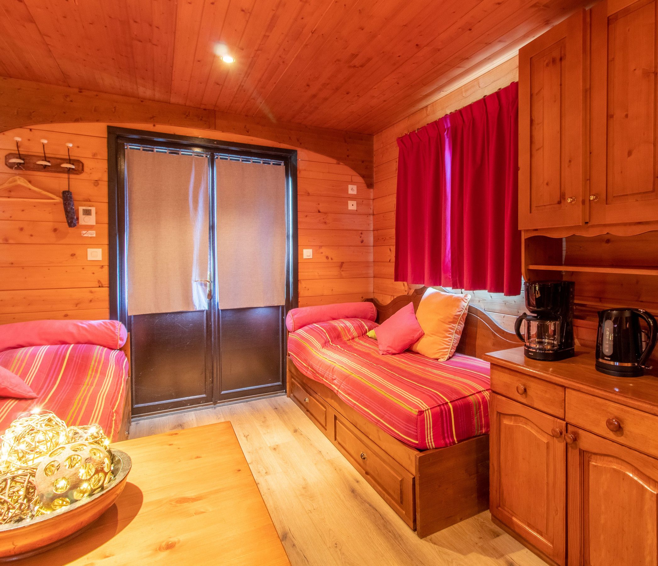 A cozy cabin interior with a bed, a small kitchen area, and a window with curtains.