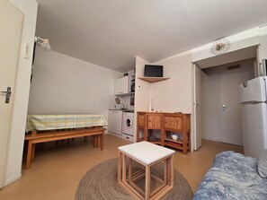 Una stanza compatta con un letto, un tavolino, una lavatrice e una TV a parete.