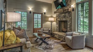 A cozy living room with a stone fireplace, large windows, and comfortable seating. - Cider Mill House overlooking private stream w/ firepit (Ellijay)
