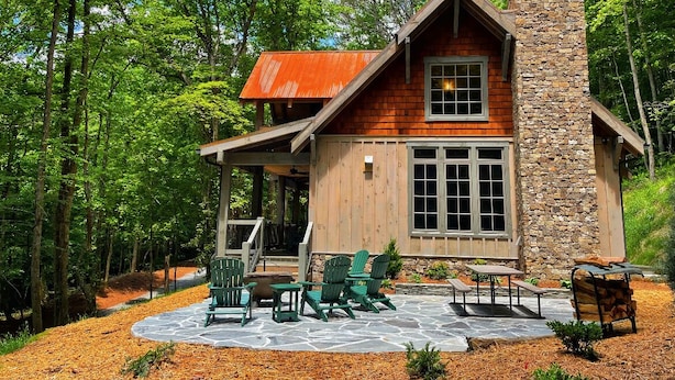 A cabin with a stone chimney, wooden exterior, and a patio with Adirondack chairs. - Cider Mill House overlooking private stream w/ firepit (Ellijay)