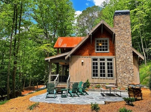 A cabin with a stone chimney, wooden exterior, and a patio with Adirondack chairs. - Cider Mill House overlooking private stream w/ firepit (Ellijay)