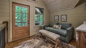 A cozy room with a wooden door, a grey sofa, a small table, and framed butterfly pictures on the wall.
