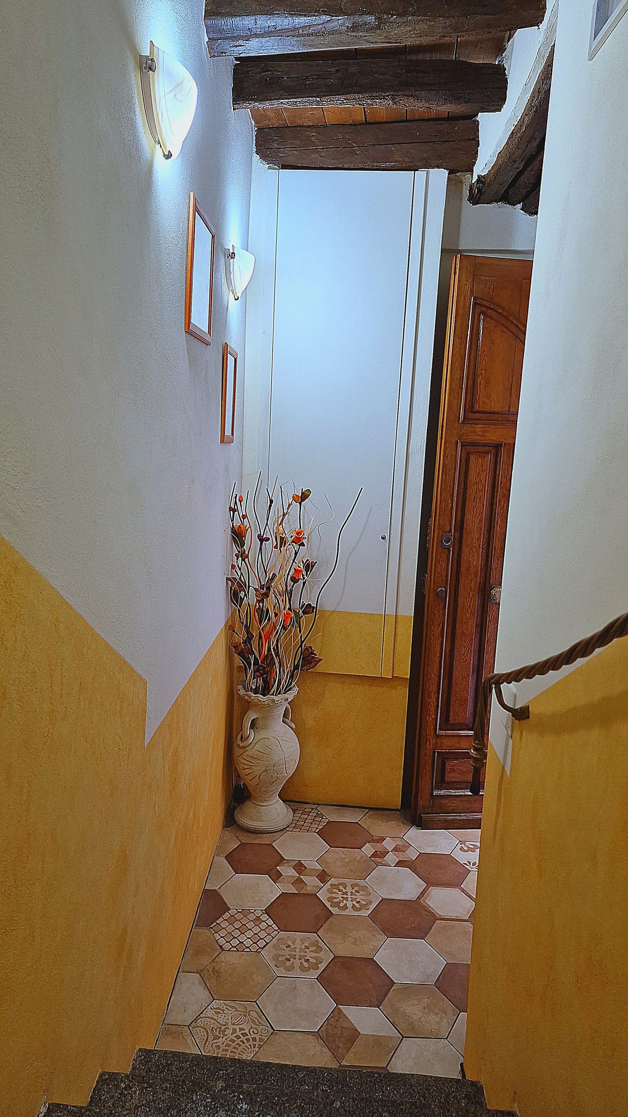 A hallway with a tiled floor, a wooden door, and a vase with branches.
