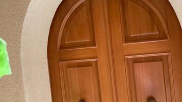 A wooden double door with a rounded arch above it, set in a beige wall.