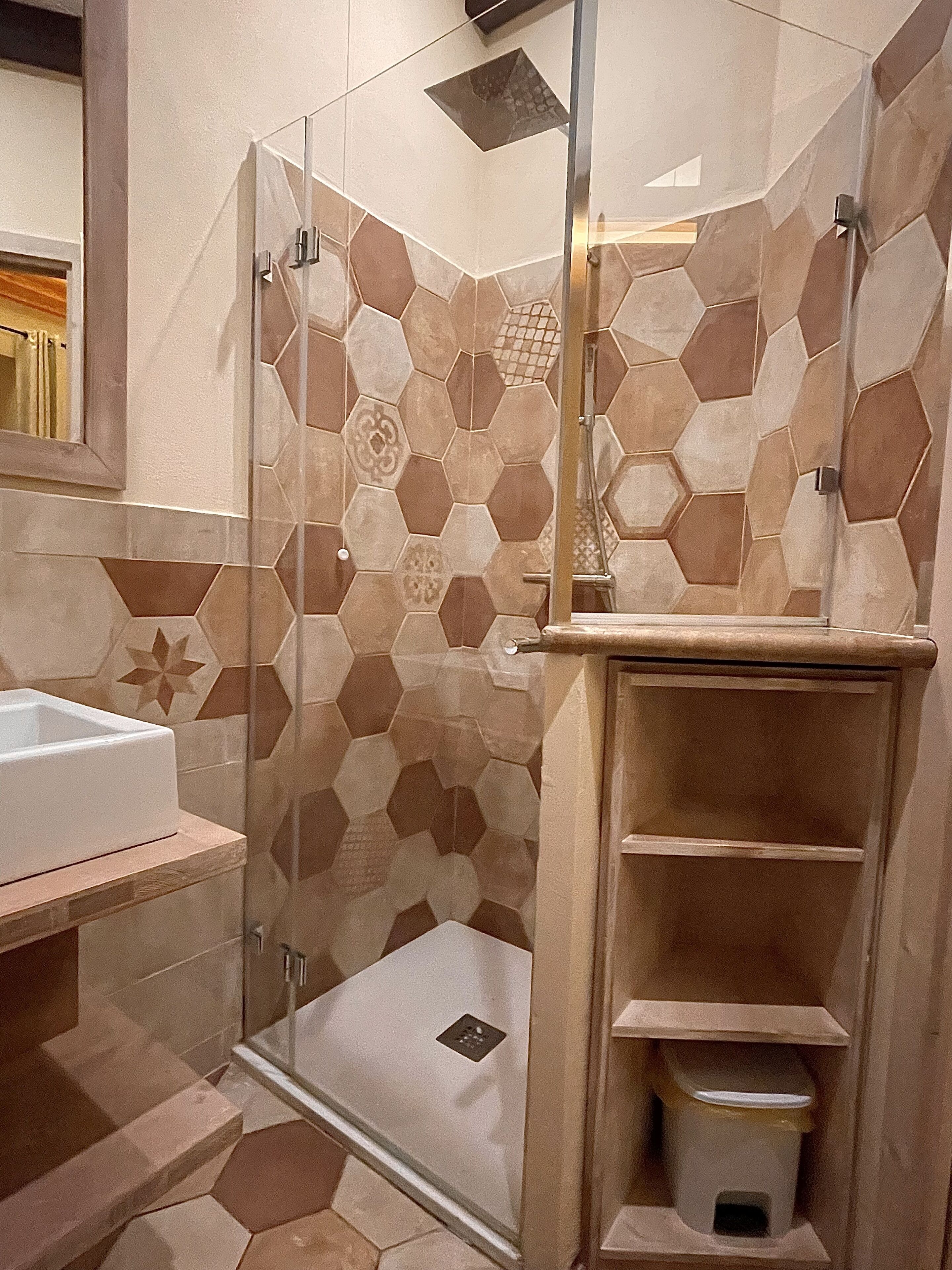A bathroom with a glass-enclosed shower, a white sink, and a tiled floor with hexagonal patterns.