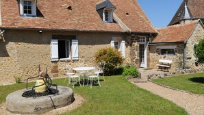 A stone house with a tiled roof, a small garden with a fire pit, and outdoor seating. - Charming Countryside Retreat: Heated Pool, Tennis, Games Room - Near Le Mans (Maresché)
