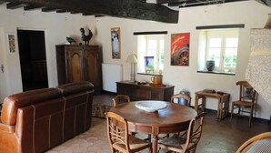 A rustic interior with a brown leather sofa, wooden dining table with chairs, and a kitchen area with a cabinet and window. - Charming Countryside Retreat: Heated Pool, Tennis, Games Room - Near Le Mans (Maresché)