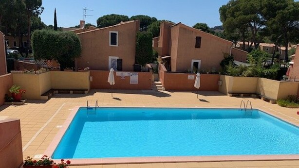 Ein rechteckiger Pool mit Fliesen umgeben, mit einer Terrassenterrasse, umgeben von Gebäuden aus Terrakotta mit kleinen Fenstern und Balkonen.