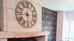 Une pièce dotée d’une grande horloge murale, d’une cheminée avec un poêle à bois et d’un papier peint à motifs.